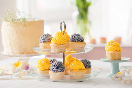 Dessert stands with tasty cupcakes, cake and flowers on table