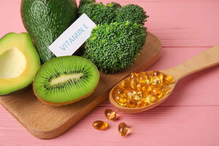Board with healthy products rich in vitamin E and fish oil capsules on color wooden background,...