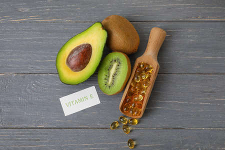 Scoop with fish oil capsules, avocado and kiwi on color wooden background