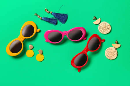 Stylish sunglasses and earrings on color background