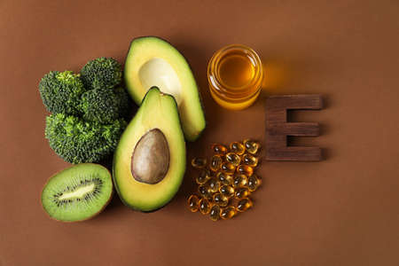 Healthy products rich in vitamin E and fish oil capsules on color background