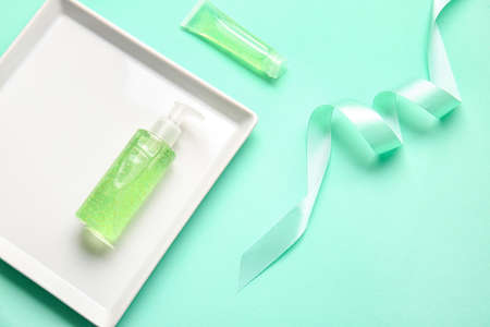 Plate with cosmetic products and ribbon on color background