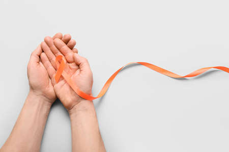 Male hands with orange ribbon on light background. Cancer leukemia awareness concept