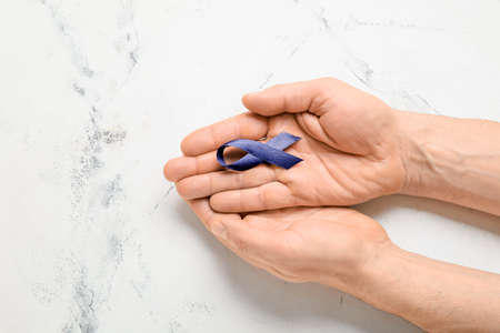 Male hands with blue ribbon on light background. Colon cancer conceptの写真素材