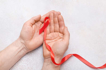 Male hands with red ribbon on light background, closeup. Cancer aids awareness conceptの写真素材