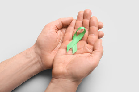Male hands with green ribbon on light background, closeup. Mitochondrial diseases and kidney cancer...