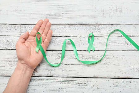 Male hand with green ribbons on light wooden background. Mitochondrial diseases and kidney cancer conceptの写真素材