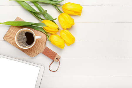 Cup of coffee and tulips on light wooden background