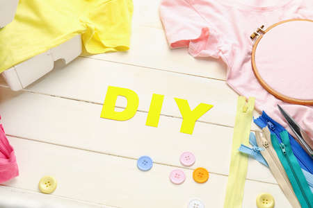 Composition with word DIY, buttons and clothes on white wooden background