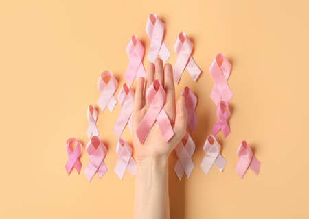 Female hand with pink ribbons on color background. Breast cancer concept
