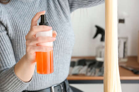 Female hairdresser spraying strand of blonde hair in beauty salon, closeupの写真素材