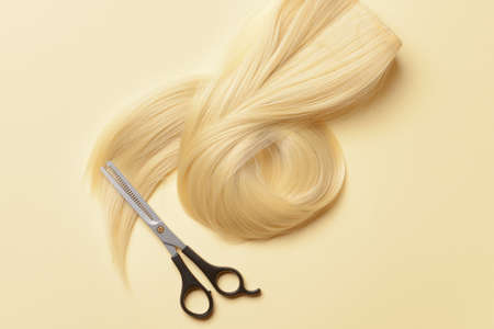 Strand of blonde hair with scissors on color backgroundの写真素材