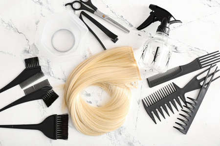 Barber's tools and strand of blonde hair on light background
