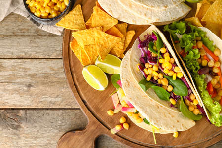 Board with tasty vegetarian tacos and nachos on wooden backgroundの写真素材