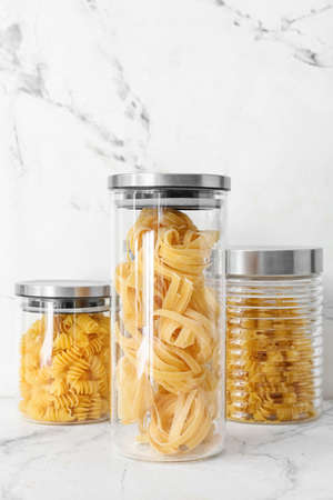 Glass jars with raw pasta on light background