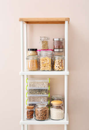 Jars and containers with different products on shelves near color wall