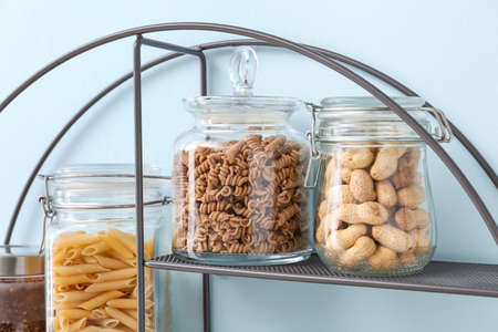 Jars with different products on shelf near color wall