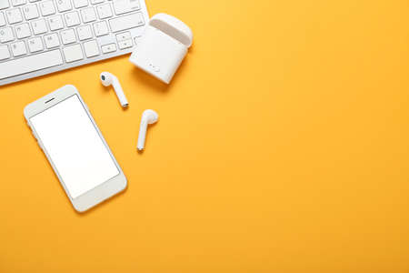 Modern earphones, mobile phone and computer keyboard on color background