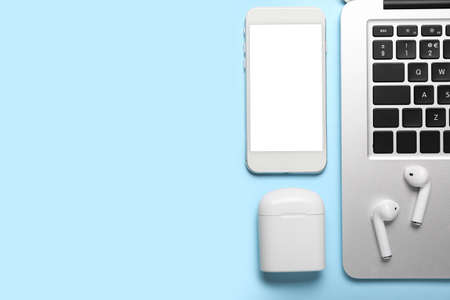 Modern earphones, laptop and mobile phone on color background