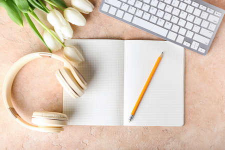 Modern headphones, computer keyboard, notebook and tulips on color background