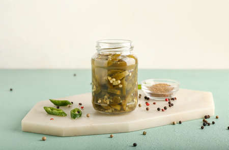 Glass jar with canned jalapeno on color background