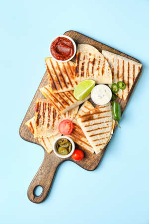 Board with tasty quesadillas, lime and sauces on color background
