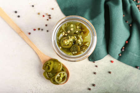 Glass jar and wooden spoon with canned jalapeno on light backgroundの写真素材