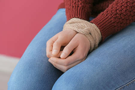 Female hostage with tied hands sitting on chair in room, closeup