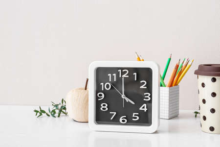 Stylish clock with pencils on table near light wall