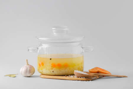 Stylish cooking pot with hot soup and ingredients on light backgroundの写真素材