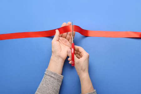 Woman cutting red ribbon on color backgroundの写真素材