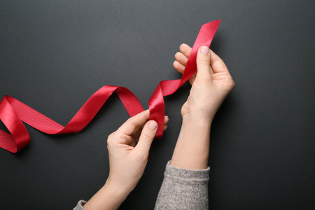 Female hands with red ribbon on dark backgroundの写真素材