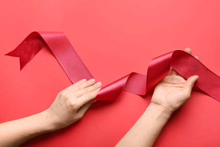 Female hands with red ribbon on color backgroundの写真素材