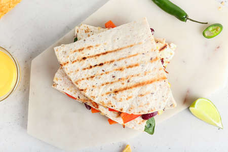 Board with tasty vegetarian quesadillas on light background
