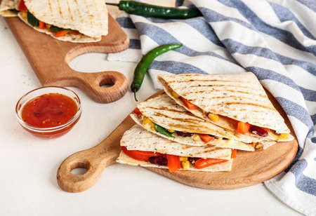 Boards with tasty vegetarian quesadillas and sauce on light background