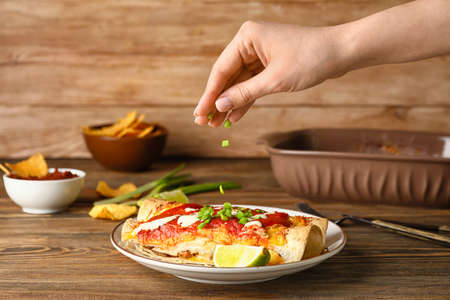 Woman adding green onion to tasty enchilada on plateの写真素材