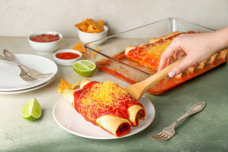 Woman putting hot enchilada from baking dish onto plateの写真素材
