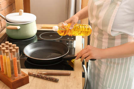Woman pouring sunflower oil onto frying pan in kitchenの写真素材