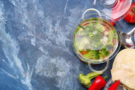 Stylish cooking pot with tasty soup and ingredients on color background
