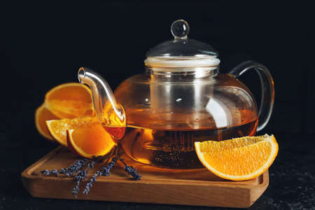 Glass tea pot with citrus beverage on dark background