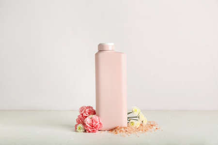 Bottle of shower gel, flowers and sea salt on light background