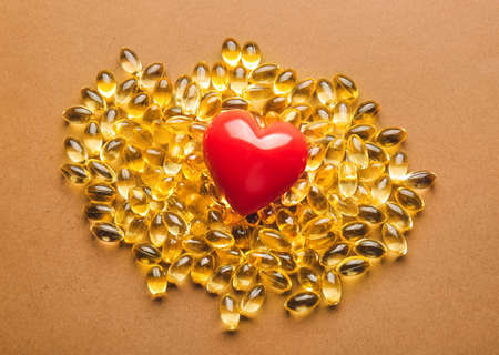 Fish oil capsules and heart on color backgroundの写真素材