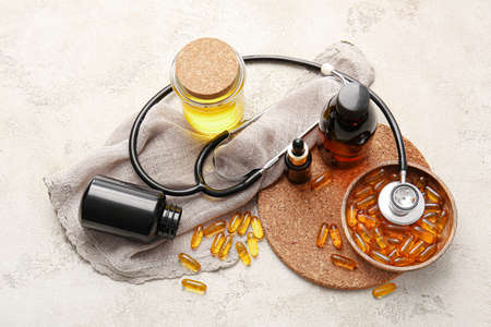 Bottles of fish oil, stethoscope and bowl with capsules on light backgroundの写真素材