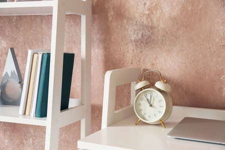 Alarm clock on table and book shelf near color wall