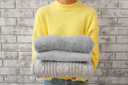 Woman with stack of stylish clothes on brick background