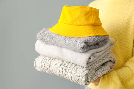 Woman with stack of stylish clothes and hat on gray backgroundの写真素材