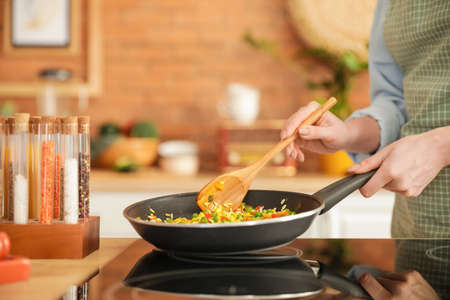 Woman cooking tasty rice with vegetables on stove in kitchen, closeupの写真素材
