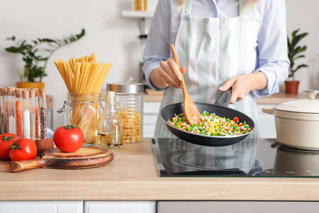 Woman cooking tasty rice with vegetables on stove in kitchen, closeupの写真素材