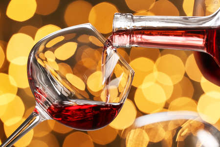 Pouring of tasty red wine into glass on blurred background, closeup