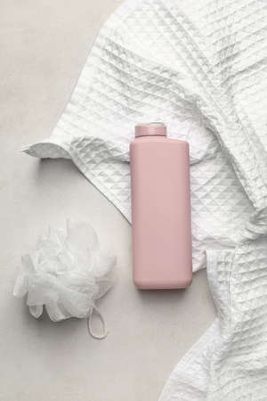 Bottle of shower gel, sponge and towel on light background